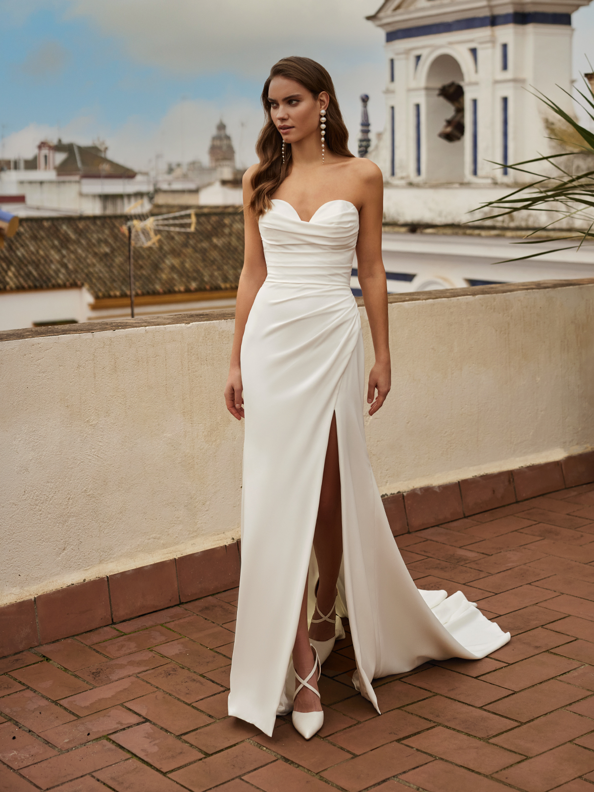 Bride outside on a balcony wearing a simple crepe bridal gown with a high leg slit