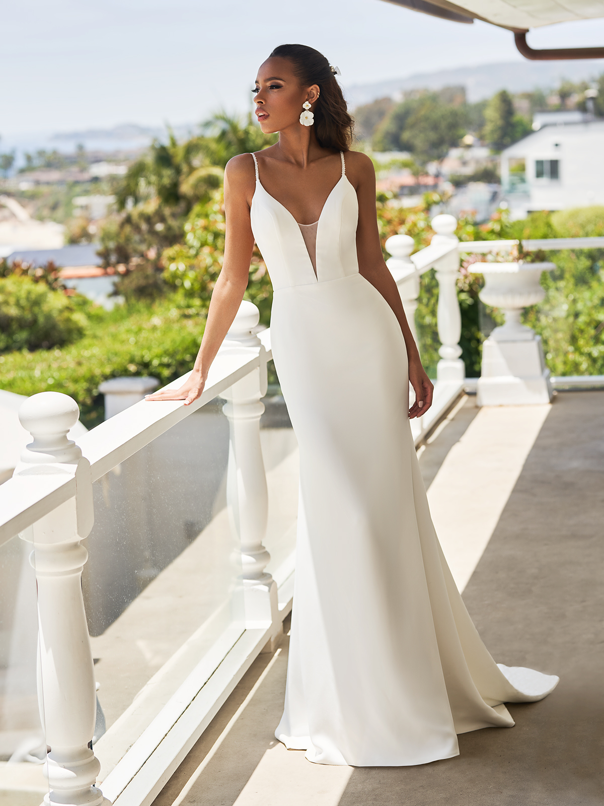 Bride leaning up against a balcony railing in a sleek crepe wedding dress