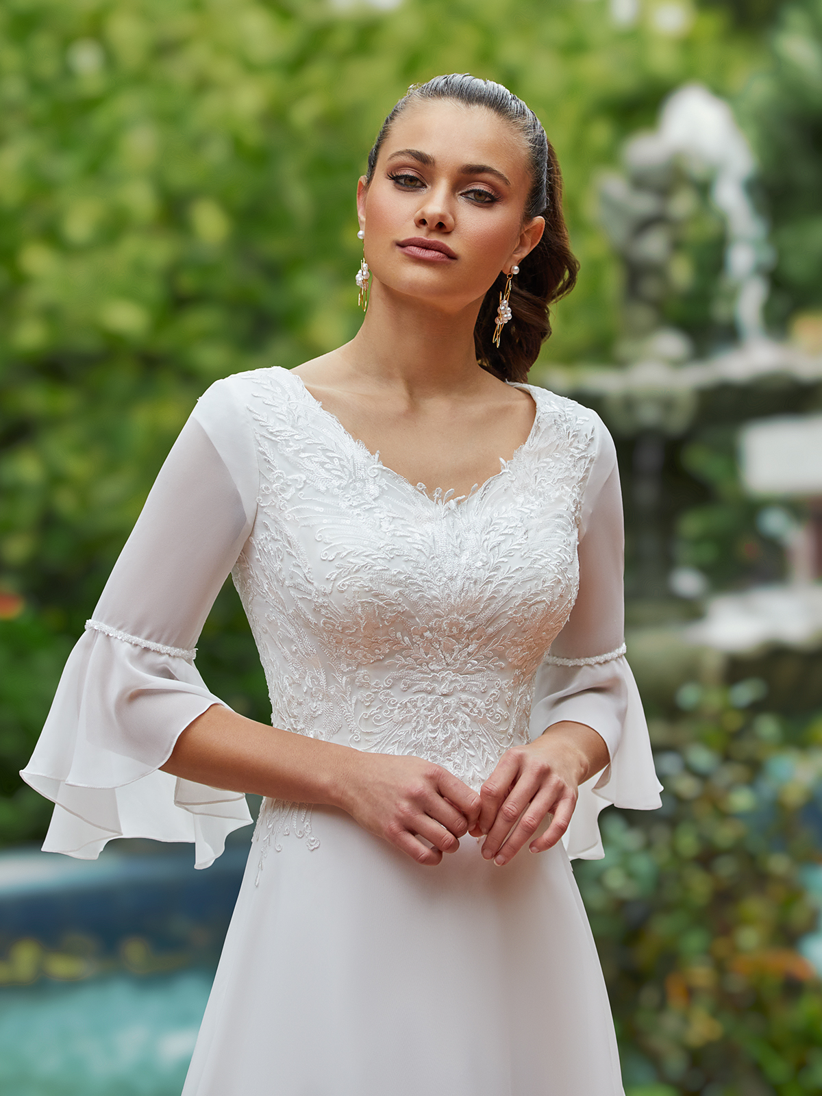 Woman standing outside in a lace and chiffon wedding gown with flowing bell sleeves