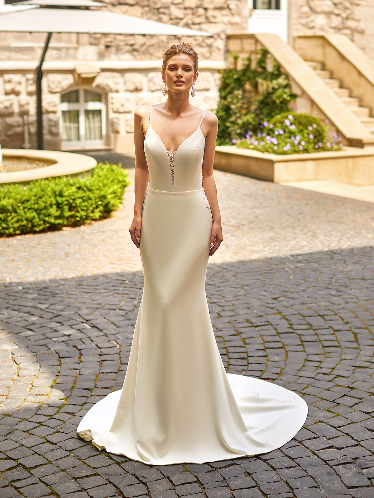 Bride standing in a courtyard wearing a crepe wedding dress with beaded spaghetti straps