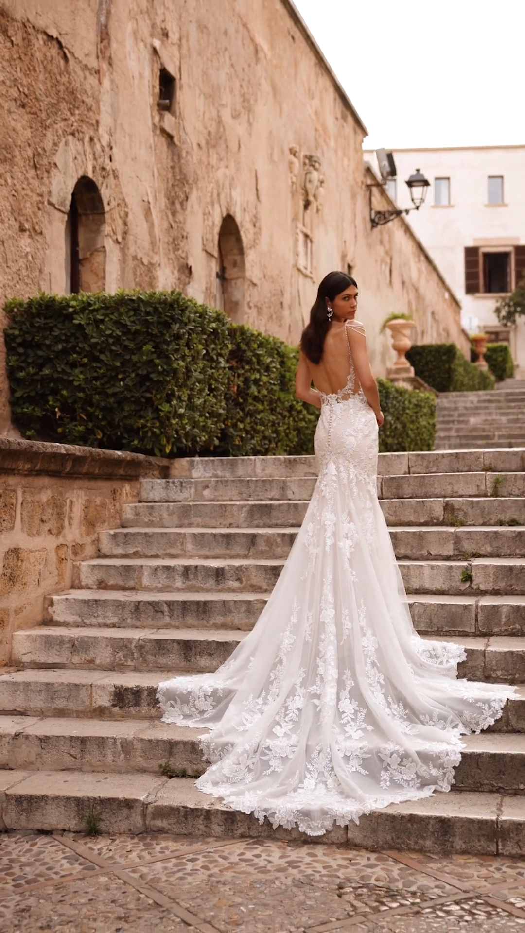Bride Walking Up Stairs in Fitted Wedding Dress With Lace Shaped Train and Low Back