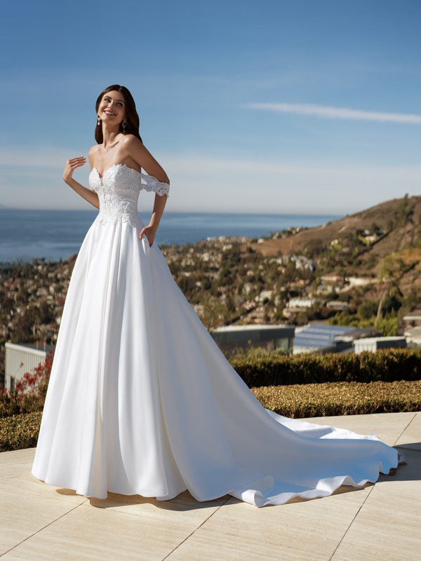 A radiant bride, donning Moonlight Couture H1588 a Mikado wedding dress, strikes a pose on a picturesque patio. The intricate beaded and lace bodice, along with the sweetheart neckline and lace swag sleeves, exude sheer beauty 