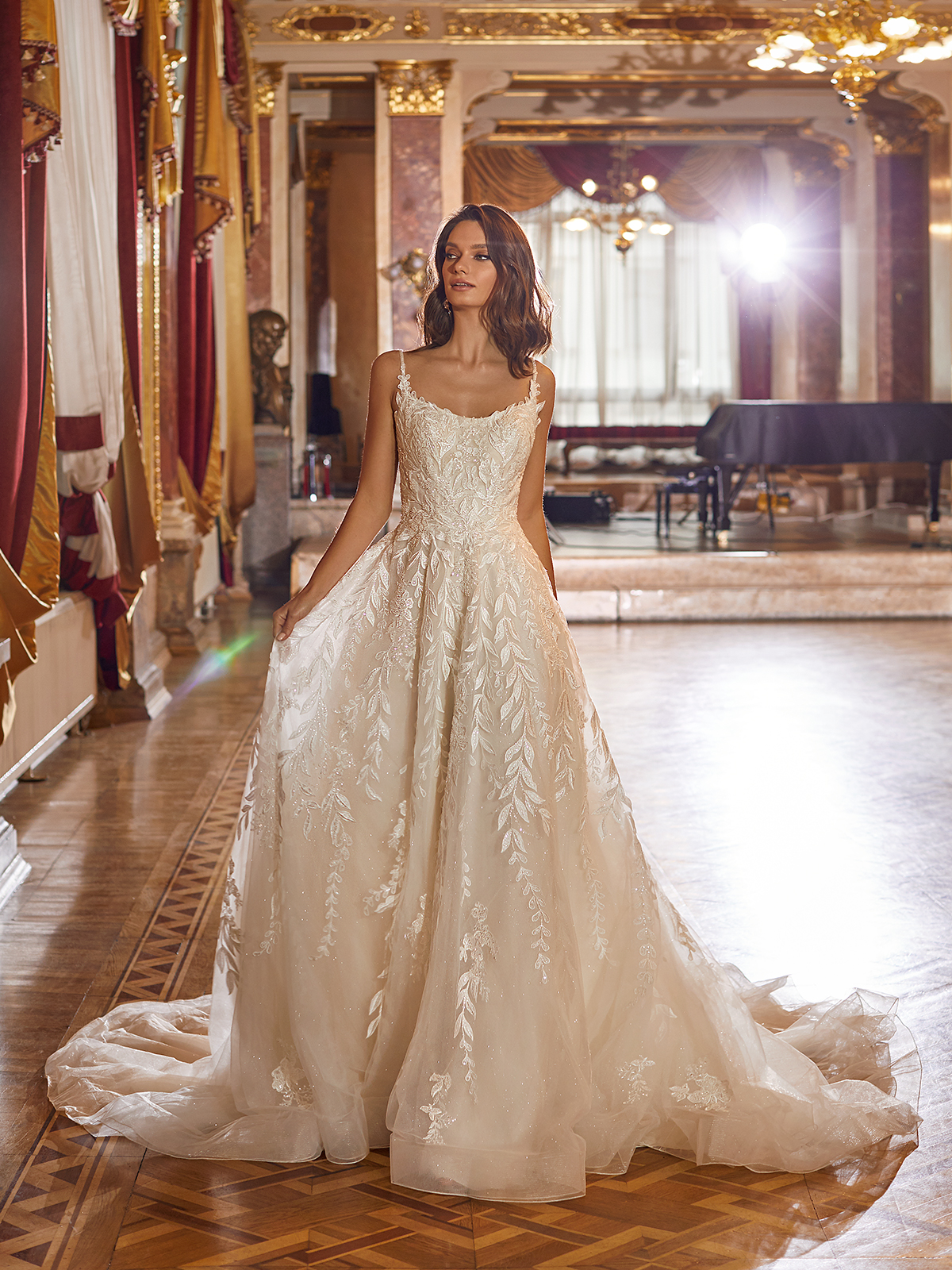 Bride in white A-line wedding gown with vine leaf lace detail standing in an elegant reception area