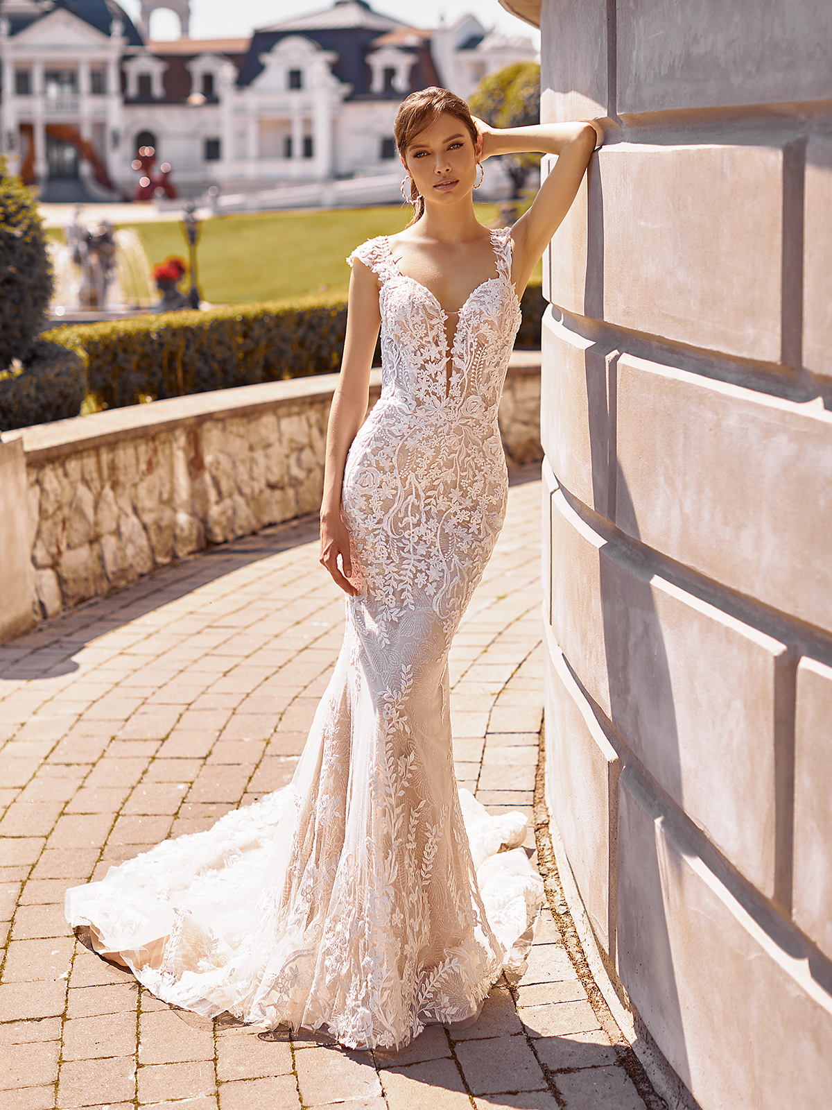 Woman standing outside of a building wearing a lace bridal gown with cap sleeves