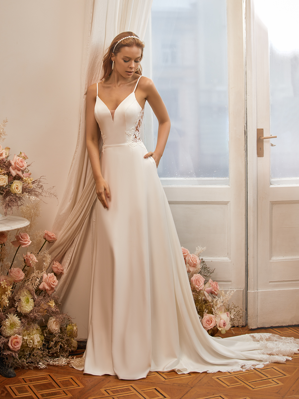 Tall bride in a crepe wedding dress standing next to a pink and white rose arrangement