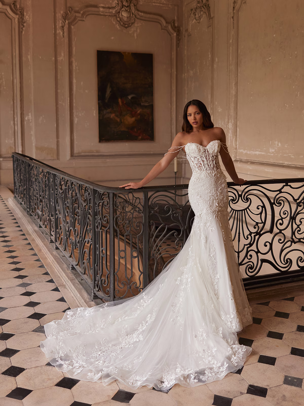 Bride leaning against an railing in a ivory wedding dress with off-the-shoulder swag sleeves