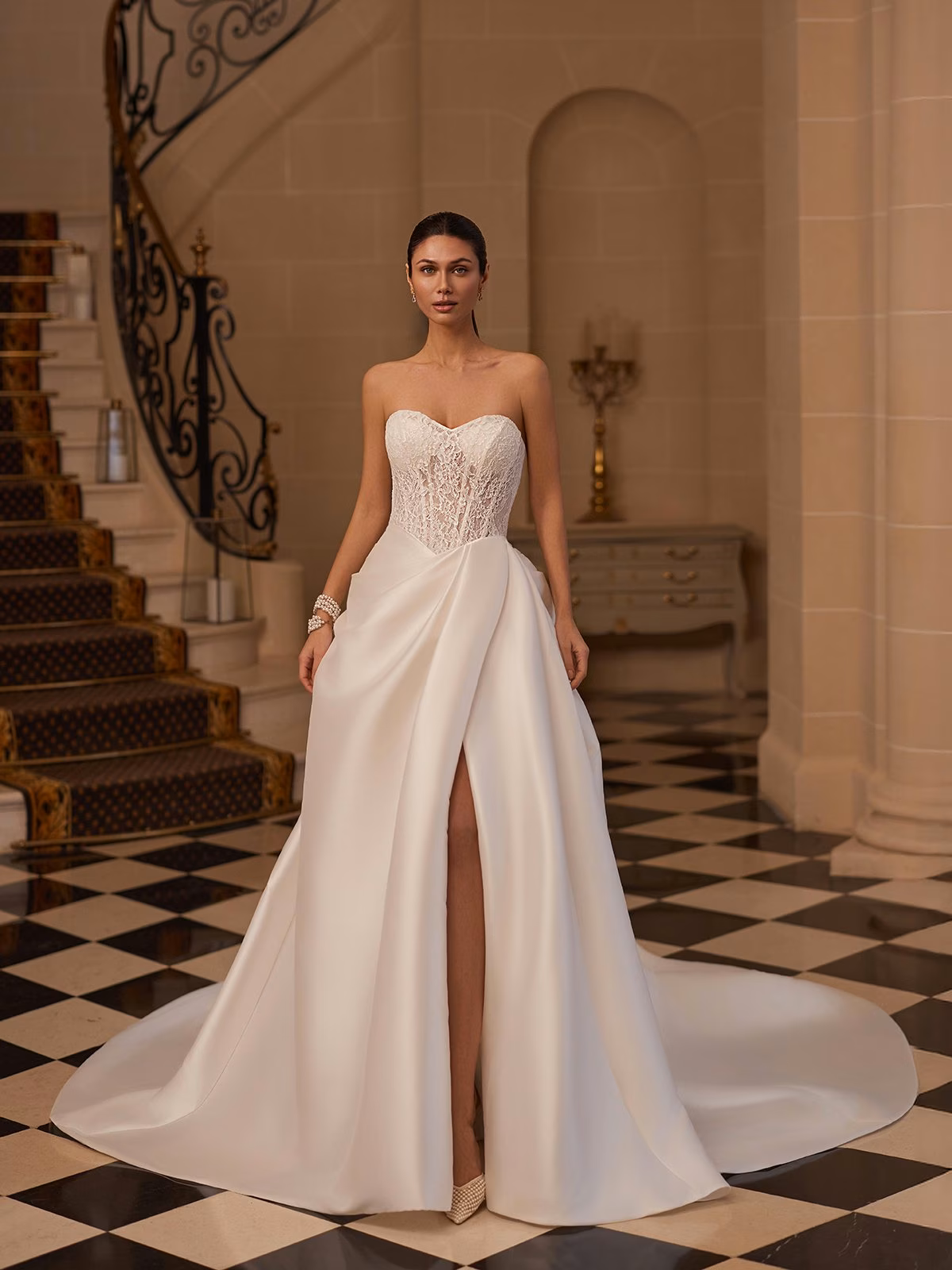 A bride in an strapless sweetheart lace bodice wedding gown with plain draped Mikado skirt stands in a luxurious hall, with a grand staircase and black-and-white checkered floor, exuding sophistication Moonlight Couture H1656