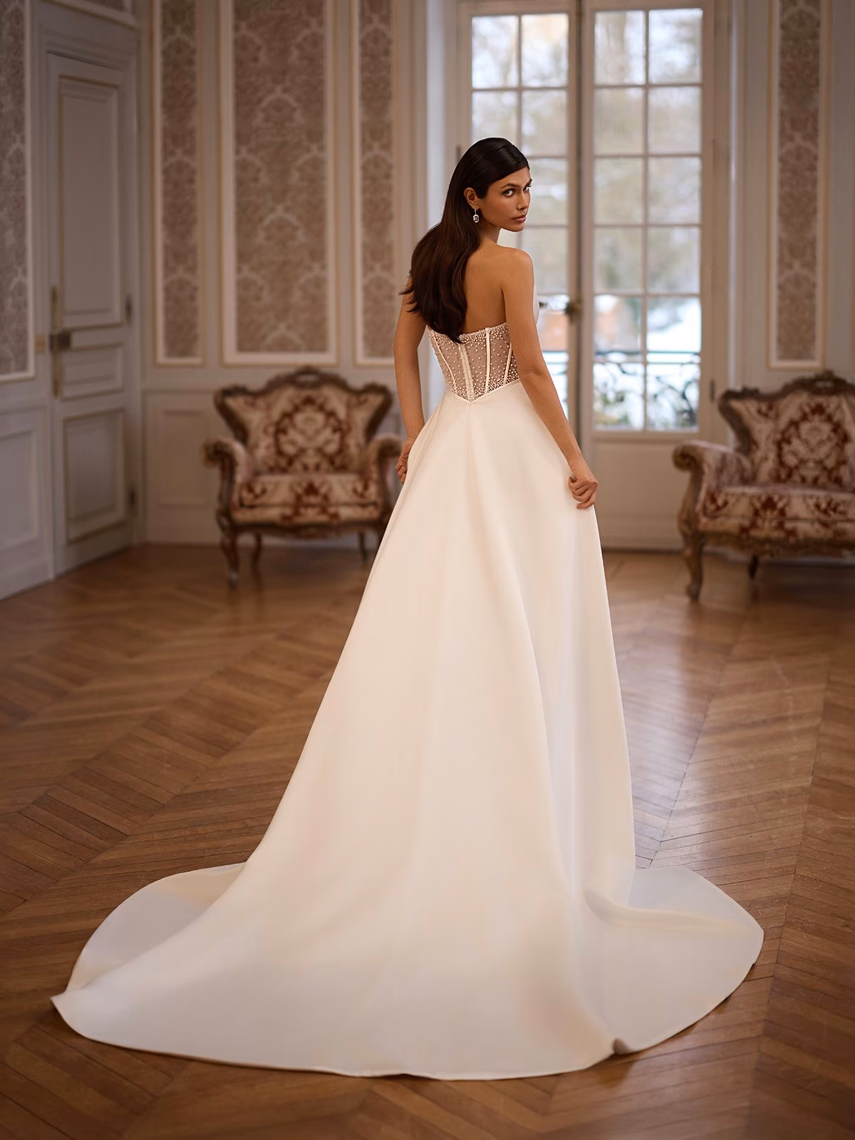 A bride wearing an Illusion open back wedding dress with beaded lace trim, stretch satin, and a long detachable train Moonlight Collection J7005