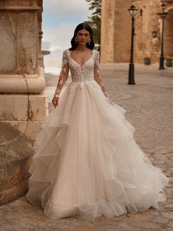 Bride Walking In A-line Wedding Dress With Cascades A Deep Plunging Sweetheart Sheer Bodice and Long Sleeves
