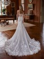 Bride stands with her back to the camera, showcasing a stunning strapless wedding gown with an intricately designed sheer corset back with pearl draping. The fitted bodice transitions seamlessly into a flowing, full-length skirt adorned with floral lace appliqués and delicate embroidery, cascading into a dramatic chapel-length train. The gown Bride stands with her back to the camera, showcasing a stunning strapless wedding gown with an intricately designed sheer corset back with pearl draping. The fitted bodice transitions seamlessly into a flowing, full-length skirt adorned with floral lace appliqués and delicate embroidery, cascading into a dramatic chapel-length train. The gown