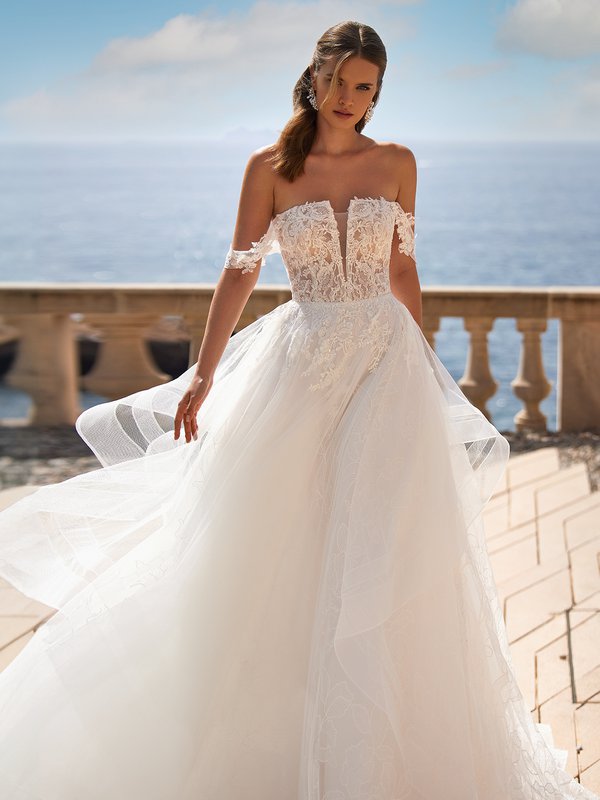 A bride wearing a straight neckline wedding dress with illusion plunge and lace bodice and off the shoulder sleeves