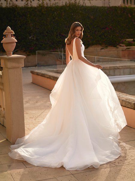 Bride walking towards stairs in a deep V-neckline Mikado bodice wedding dress with organza cascade chapel train.