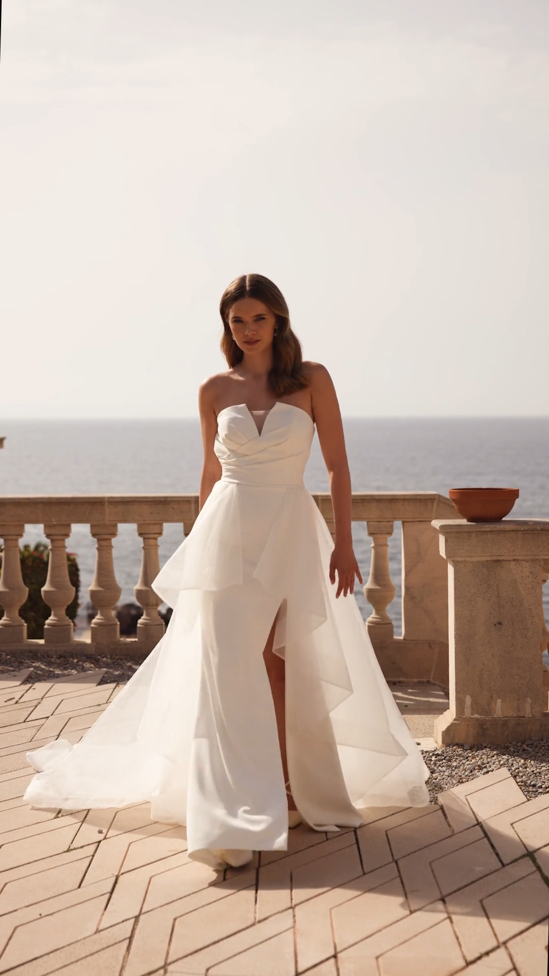 Bride outside walking in a strapless pointed sweetheart crepe wedding dress with detachable tulle train