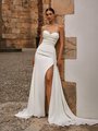 Bride leaning against wall in a sweetheart crepe wedding dress with side leg slit and side train