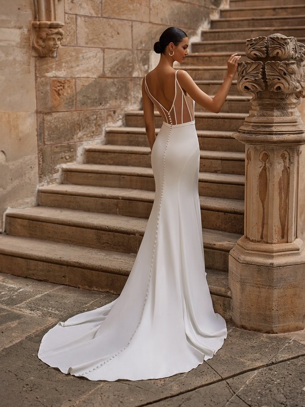 Bride standing at bottom of stairs with a low illusion back with boning details and short sweet train