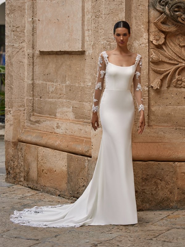 Bride leaning against building in beaded lace long sleeve wedding dress with scoop neckline